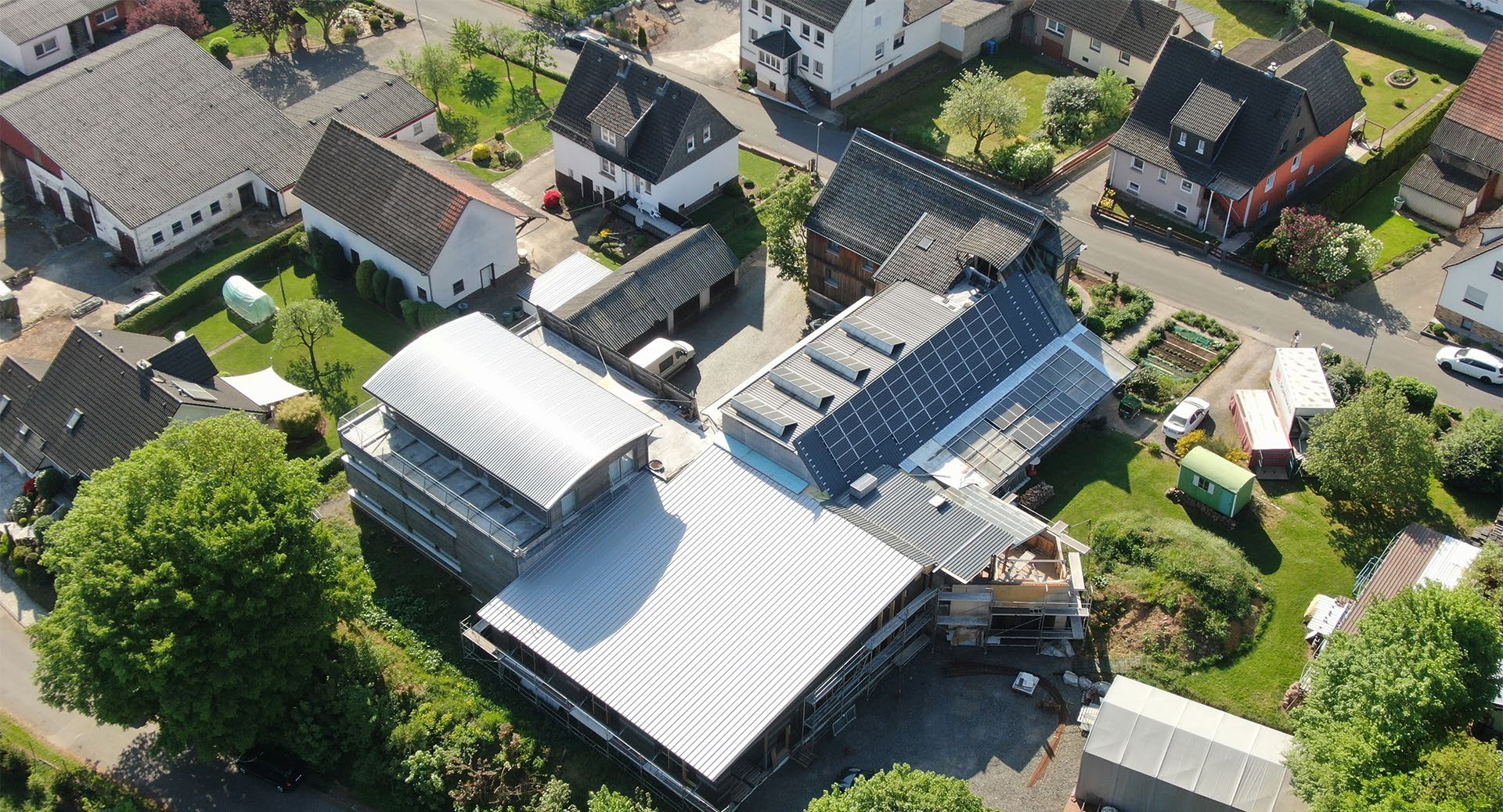 Aerial view of TWIKE 5 electric vehicle production facility in Rosenthal, showing white industrial buildings with solar panels, surrounded by residential neighborhood and green spaces