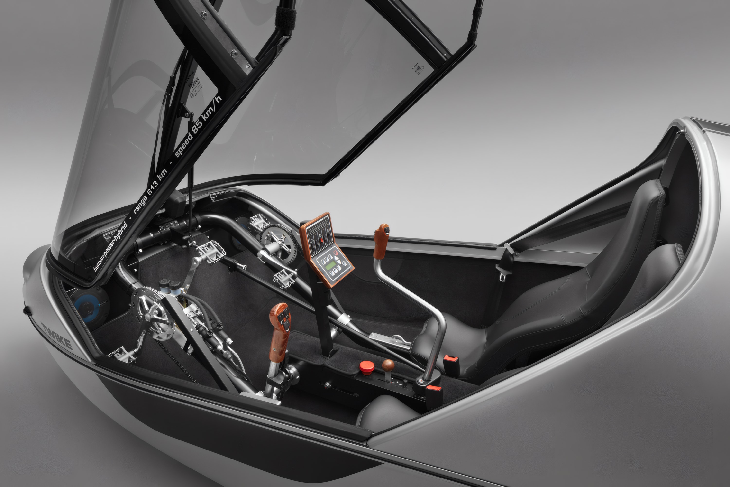 TWIKE 3 driver operating vehicle from pilot's perspective, holding orange navigation display and joystick control, open cockpit design