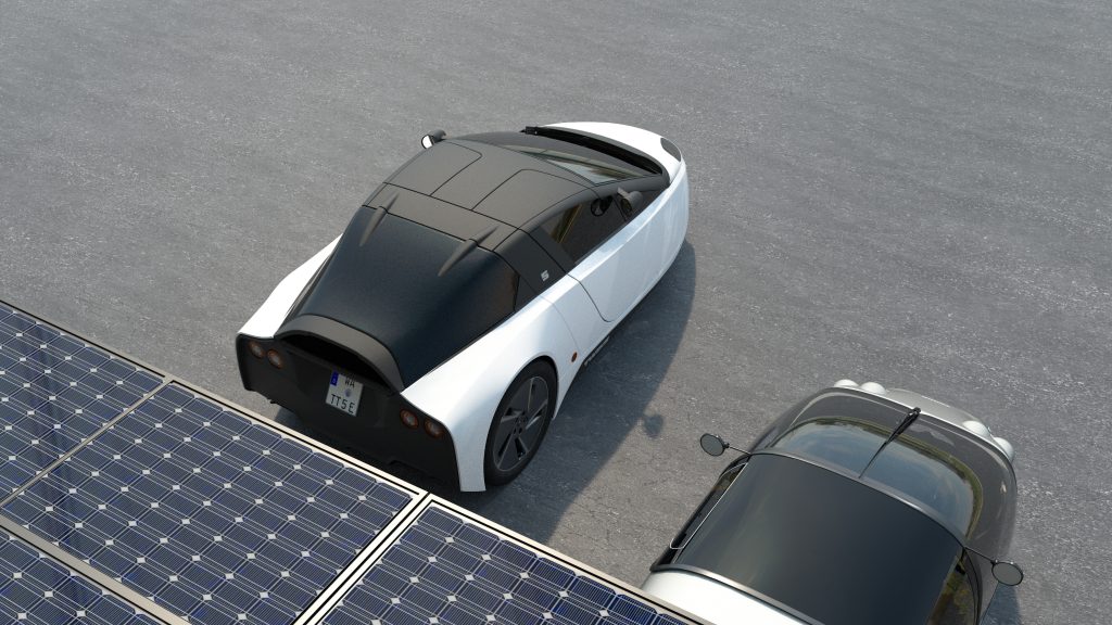 A bird's-eye view of a TWIKE 5 in white and black on gray asphalt next to solar panels.