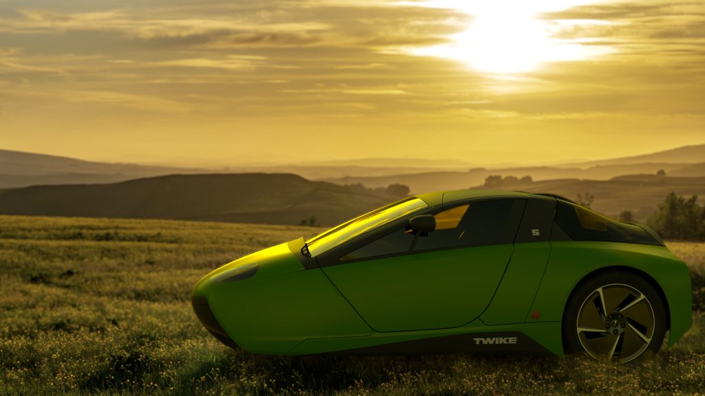 A green TWIKE 5 in a field of flowers against a hilly landscape, bathed in the golden light of the setting sun.